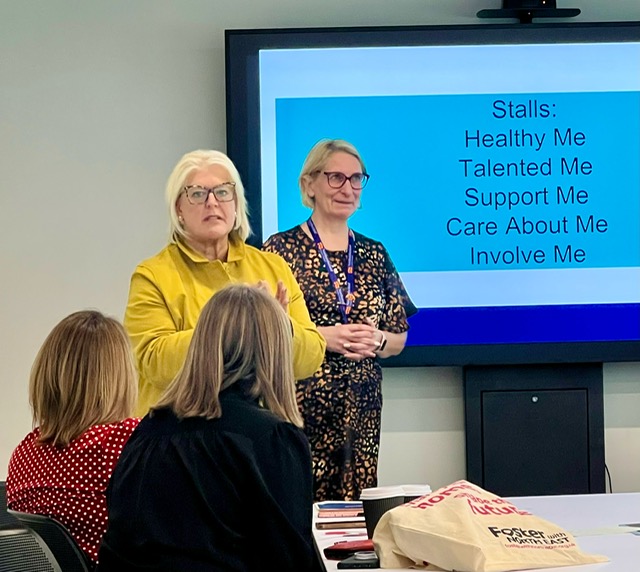 Photograph of Audrey Kingham with a colleague, standing, and two others seated in a meeting.